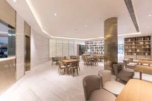 A modern interior with a central column, multiple seating areas, and a bookshelf. - Ji Hotel (Hangzhou)