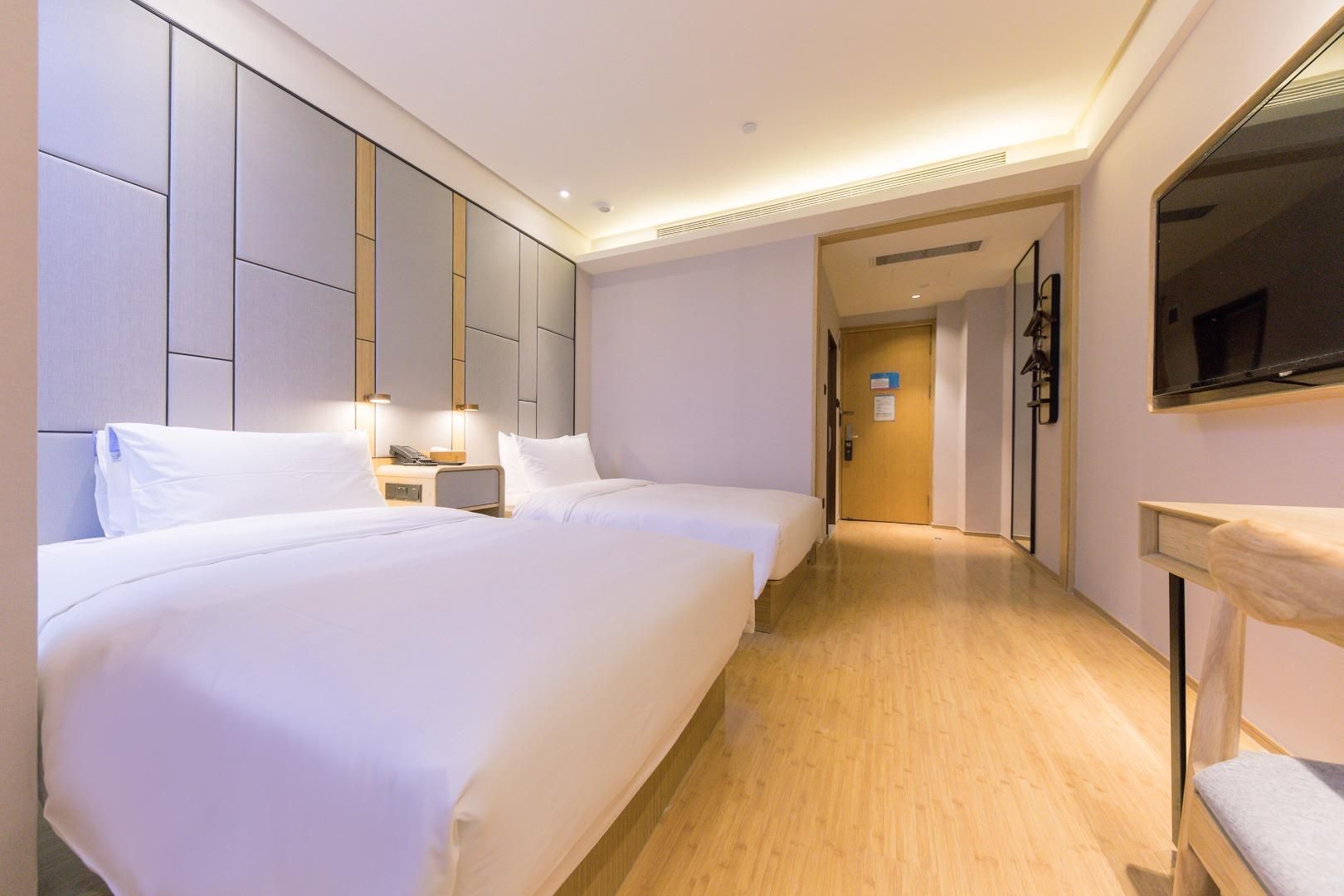 A hotel room with two beds, a bedside table, a TV, and a wooden floor.