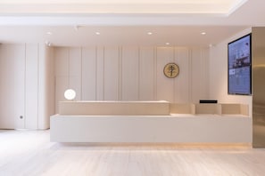 Un área de recepción moderna con diseño minimalista, que incluye un mostrador de recepción, una pantalla montada en la pared y un elemento decorativo con caracteres chinos.
