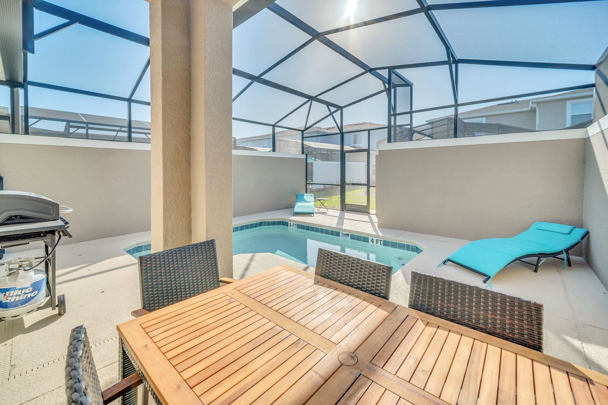 A covered outdoor area with a pool, a table with chairs, and a grill.