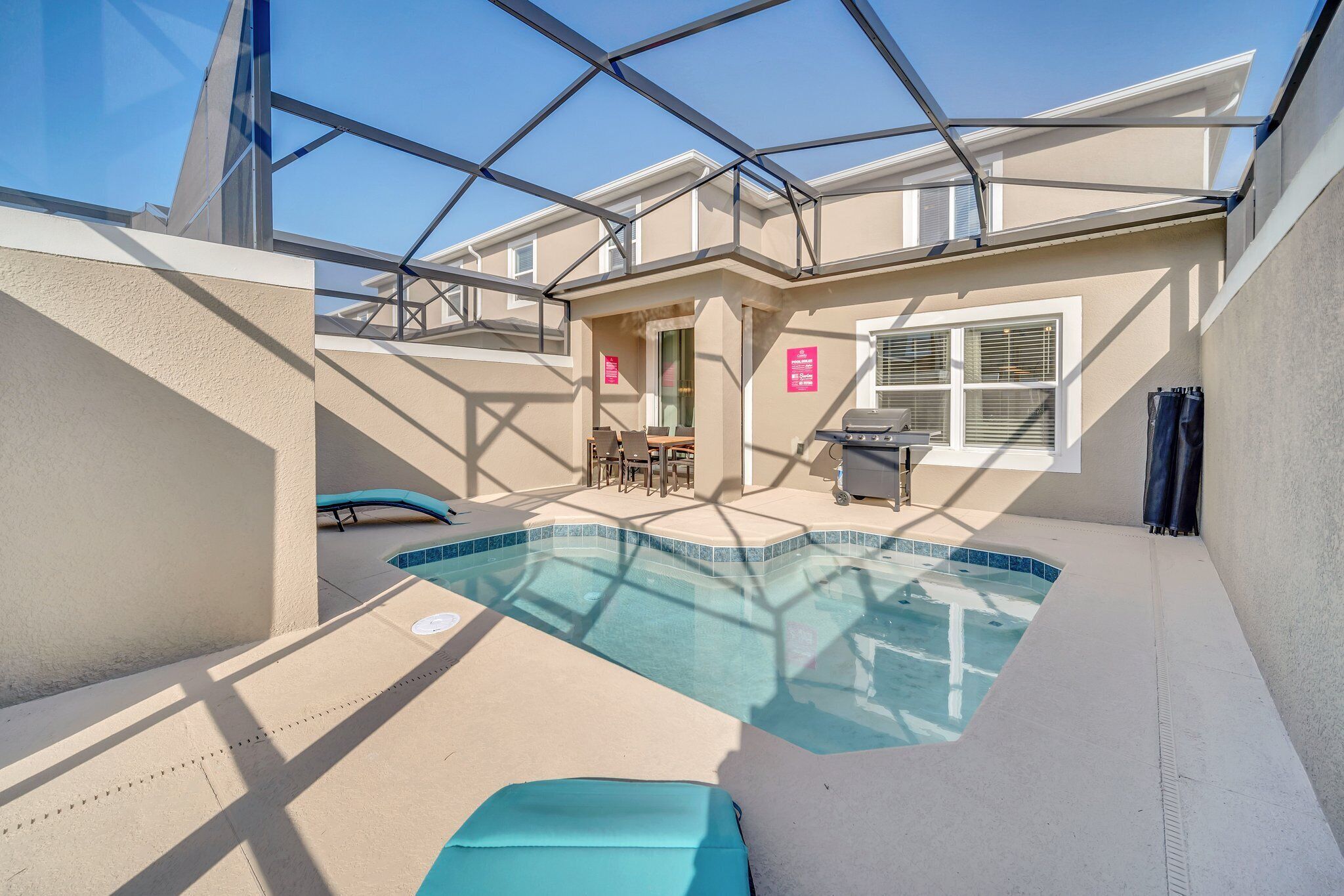 A pool area with a glass enclosure, a barbecue grill, and a seating area with tables and chairs.