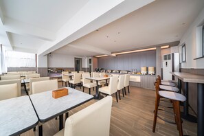 A modern dining area with tables, chairs, and a kitchen in the background.