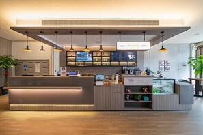 A modern coffee shop with a reception desk, digital menu boards, and pendant lighting.