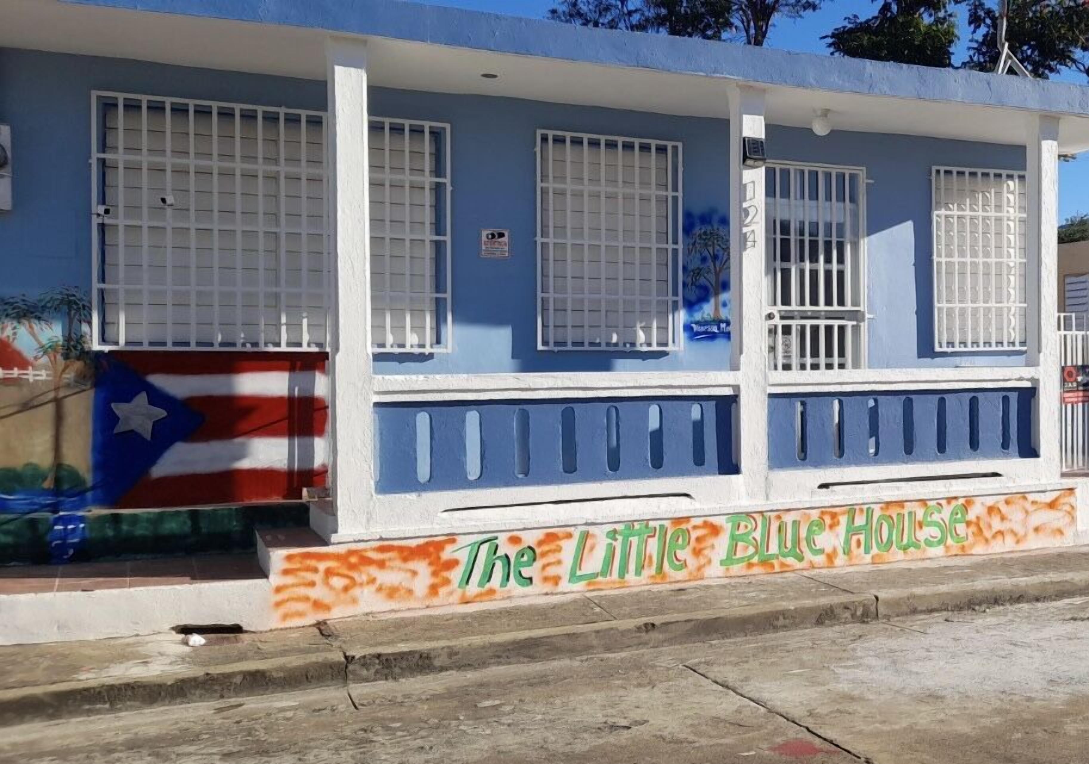 A building with a blue facade, white window bars, and a sign reading "The Little Blue House".