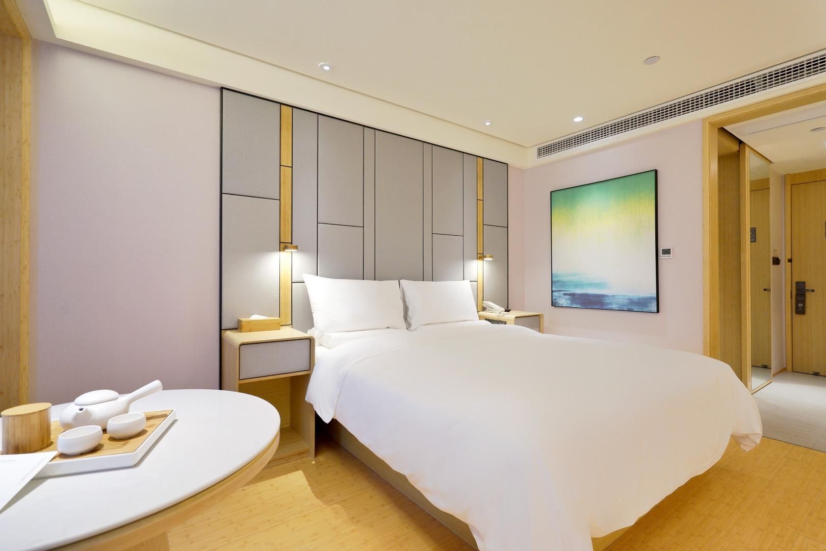 Una habitación de hotel moderna con una cama grande, mesitas de noche, una lámpara de noche, un cuadro en la pared y piso de madera.