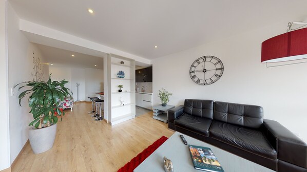 Un salon moderne avec un canapé en cuir noir, une table basse, un tapis rouge et une grande horloge murale.