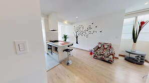 Une cuisine moderne équipée d’une cuisinière à gaz, un coin repas avec un canapé à motifs et une fresque murale représentant un arbre avec des feuilles et des oiseaux.