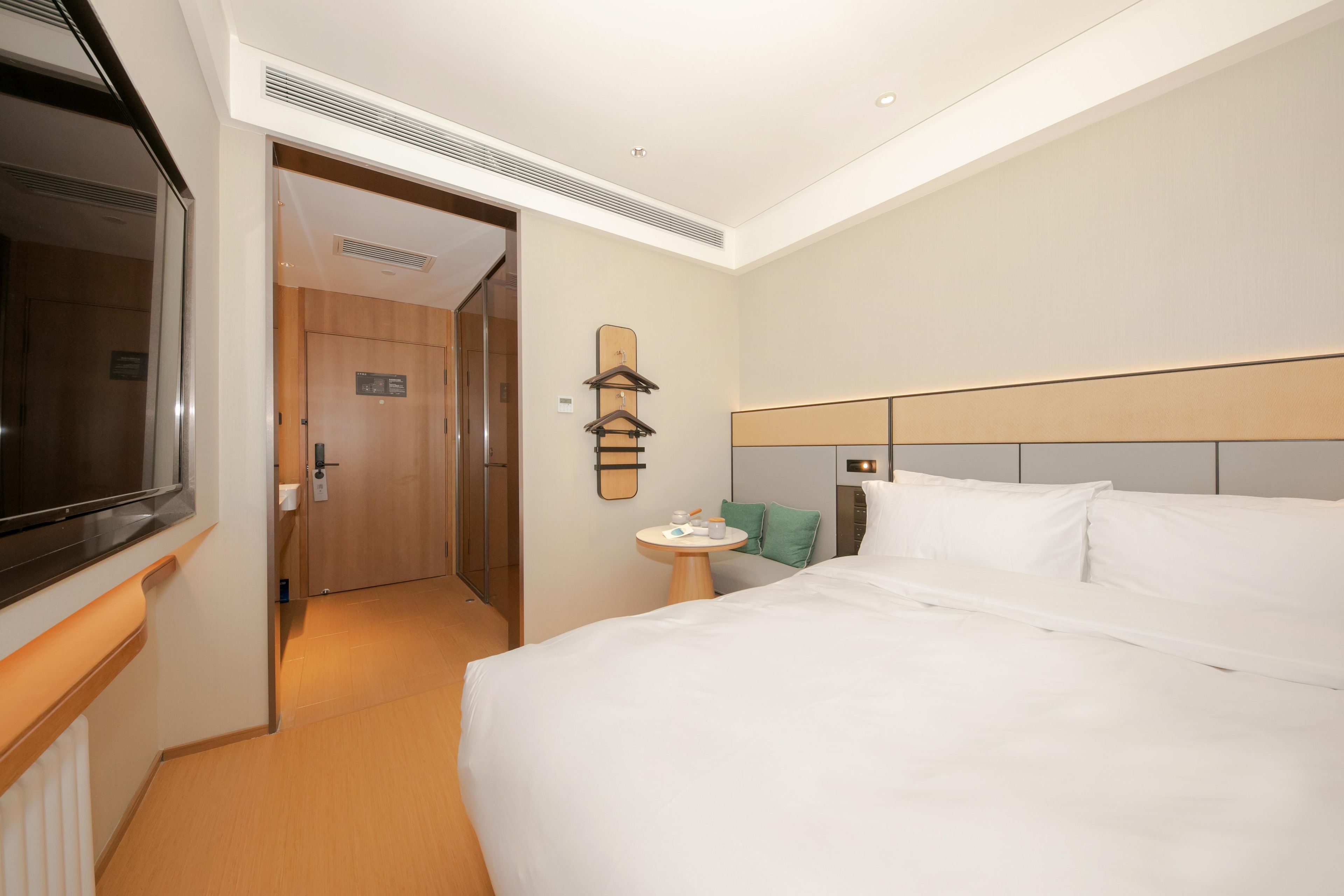 A hotel room with a bed, a bedside table, a TV, and a door leading to a bathroom.