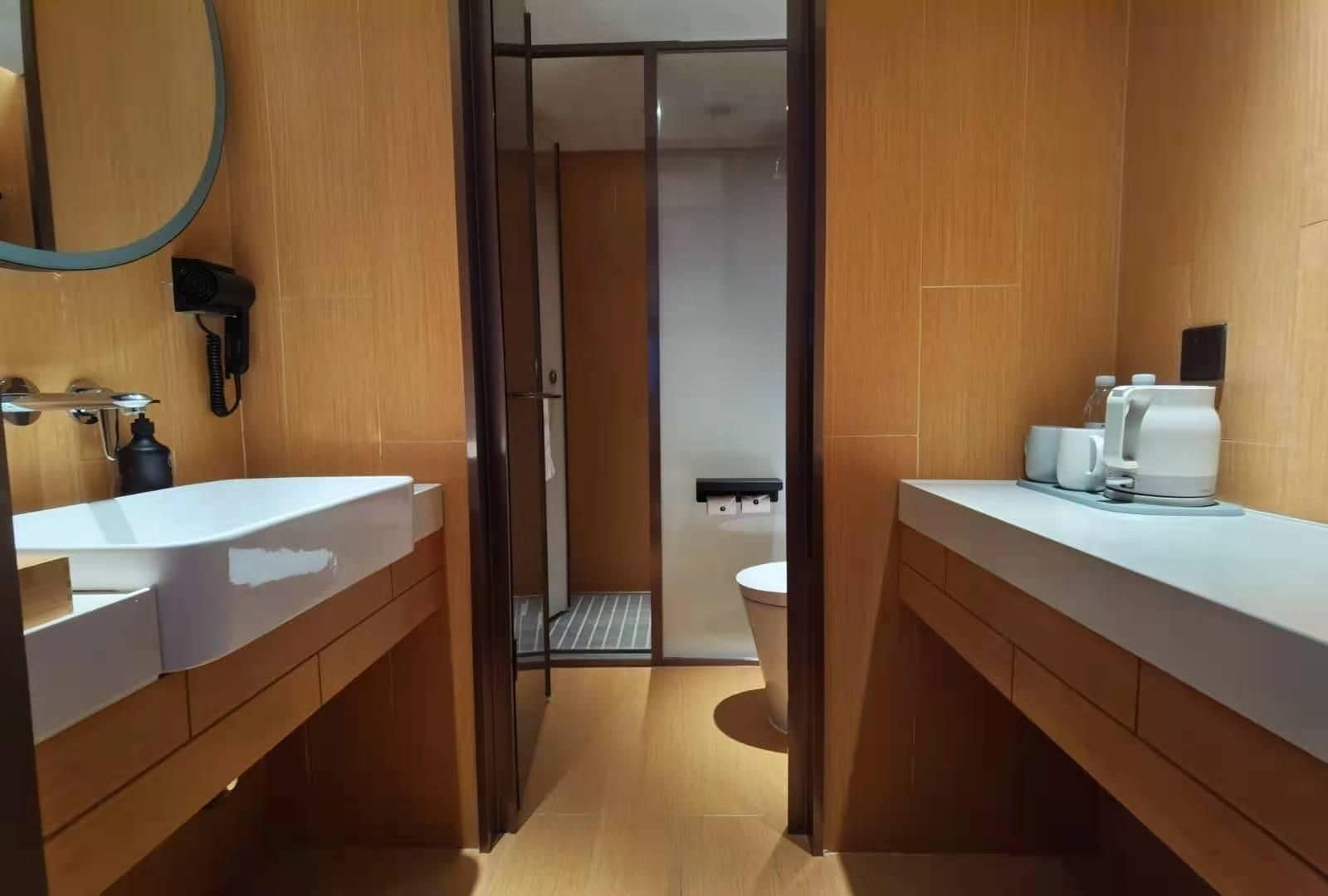 A modern bathroom with a wooden vanity, a sink, a mirror, and a shower area.