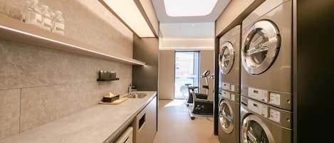 Un lavadero con varias lavadoras, un lavabo y una ventana que proporciona luz natural.