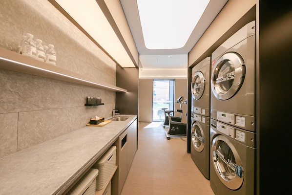 A laundry room with multiple washing machines, a sink, and a window providing natural light. - Ji Hotel (Beijing)