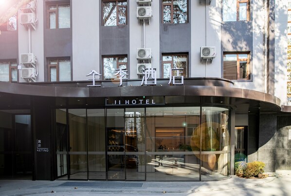 A hotel entrance with glass doors, a sign above the doors, and air conditioning units on the building facade. - Ji Hotel (Beijing)