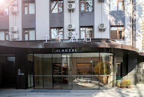 A hotel entrance with glass doors, a sign above the doors, and air conditioning units on the building facade. - Ji Hotel (Beijing)