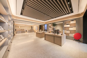 A modern interior with a reception desk, display shelves, and a large screen. - Ji Hotel (Beijing)