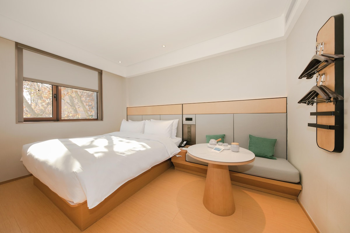 A hotel room with a bed, a round table, a sofa, and a wall-mounted clock.