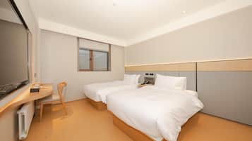Een hotelkamer met twee bedden, een bureau, een stoel, een televisie en een raam.