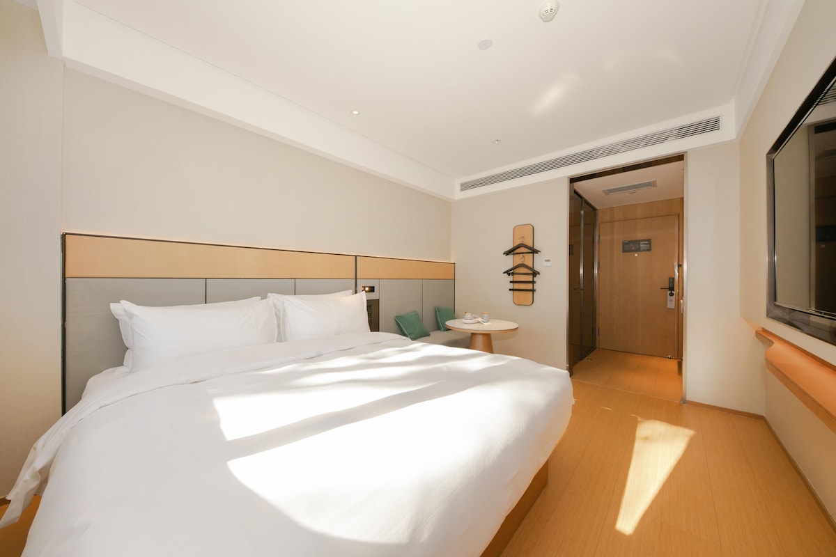 A hotel room with a large bed, a bedside table, a wall-mounted TV, and a door leading to a hallway.