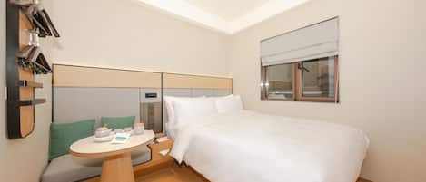 A hotel room with a bed, a small table with tea set, a mirror, and a window with blinds.