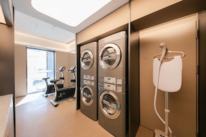 A hotel laundry room with four washing machines, a telephone, and an exercise bike. - Ji Hotel (Beijing)