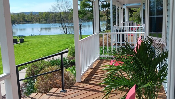 A covered deck with a view of a lake, outdoor seating, and a potted plant. - Fisher's Flop - A Lofted Condo on the Wisconsin River (Poynette)