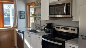 A modern kitchen with white cabinets, a stainless steel dishwasher, a black stove, and a microwave. - Fisher's Flop - A Lofted Condo on the Wisconsin River (Poynette)