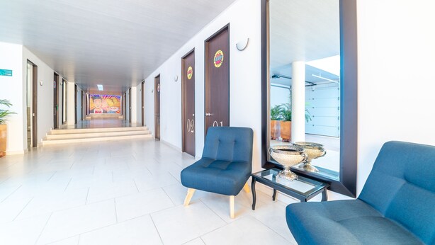 Un vestíbulo de hotel con un largo pasillo, zonas de estar azules y un amplio ventanal con vistas al exterior.