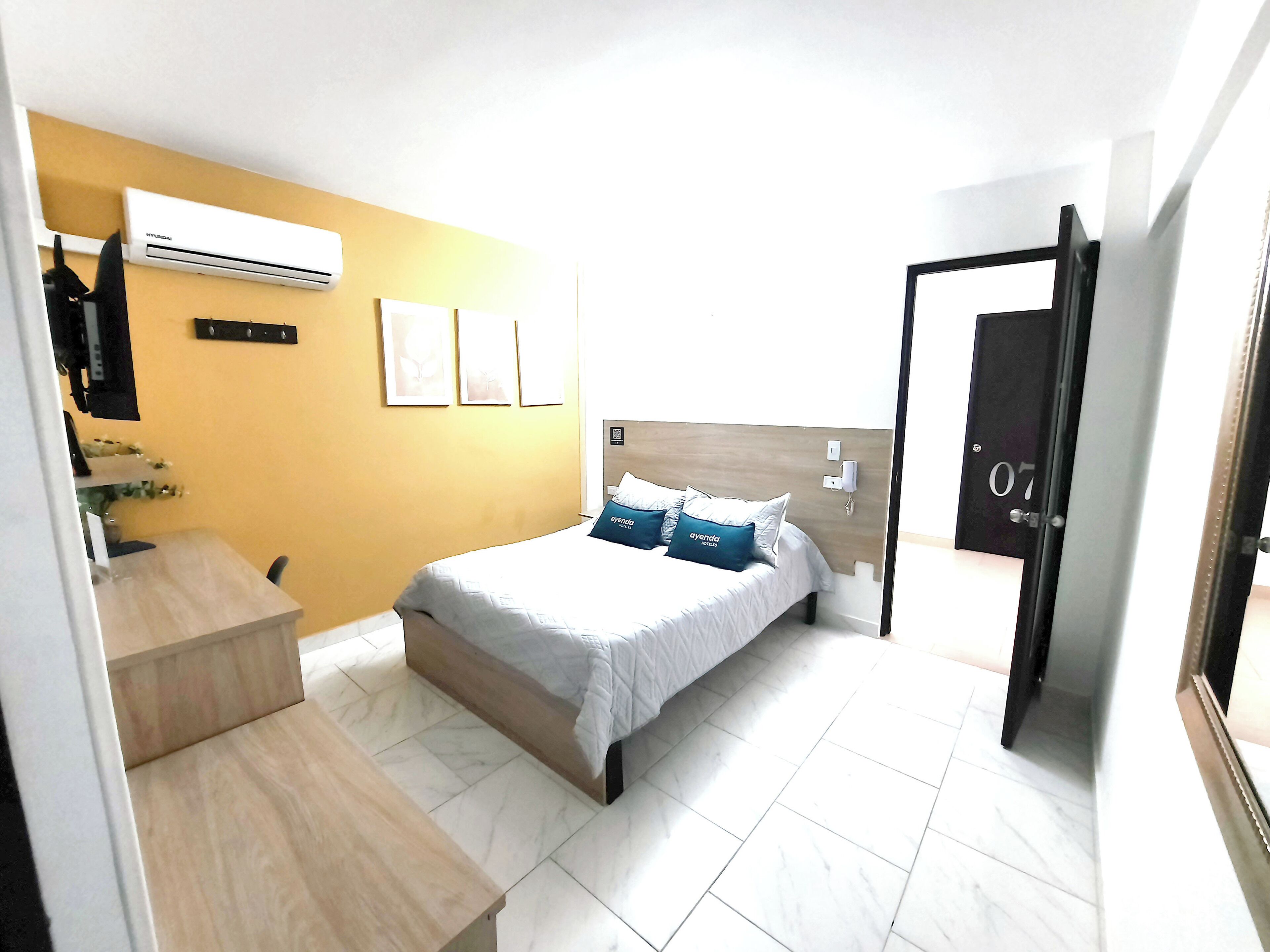 Habitación de hotel con cama, escritorio, aire acondicionado y una puerta con un número.
