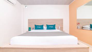Una habitación de hotel moderna con cabecera de madera, colcha gris y almohadas color turquesa que muestran el nombre del hotel.