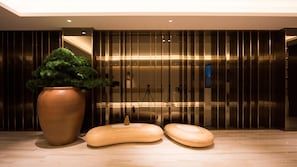 A modern interior with a large potted plant, wooden stools, and a sleek, reflective wall.