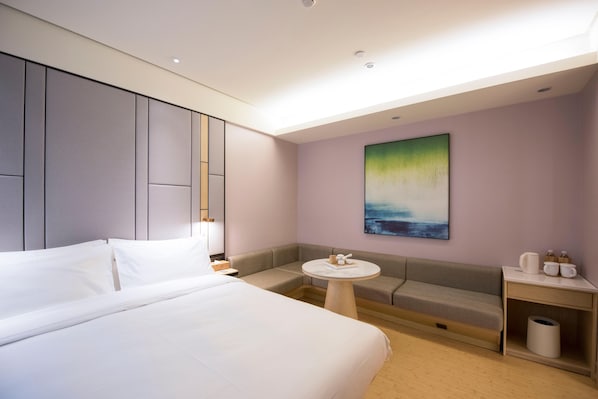 A modern hotel room with a large bed, a small round table, a sofa, and a painting on the wall.
