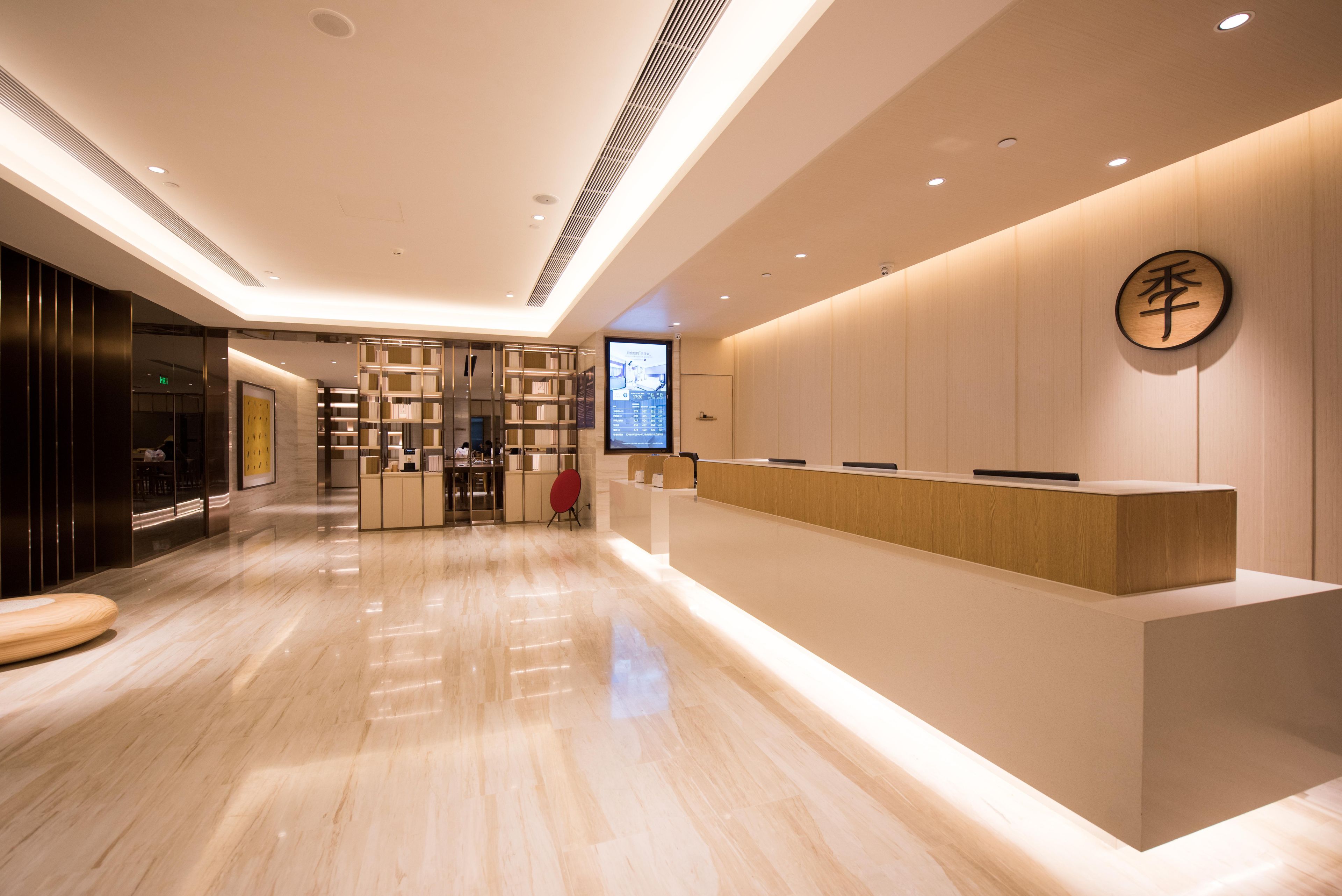 Un área de recepción de hotel moderna con un mostrador de madera, una pantalla digital y un espacio de descanso.