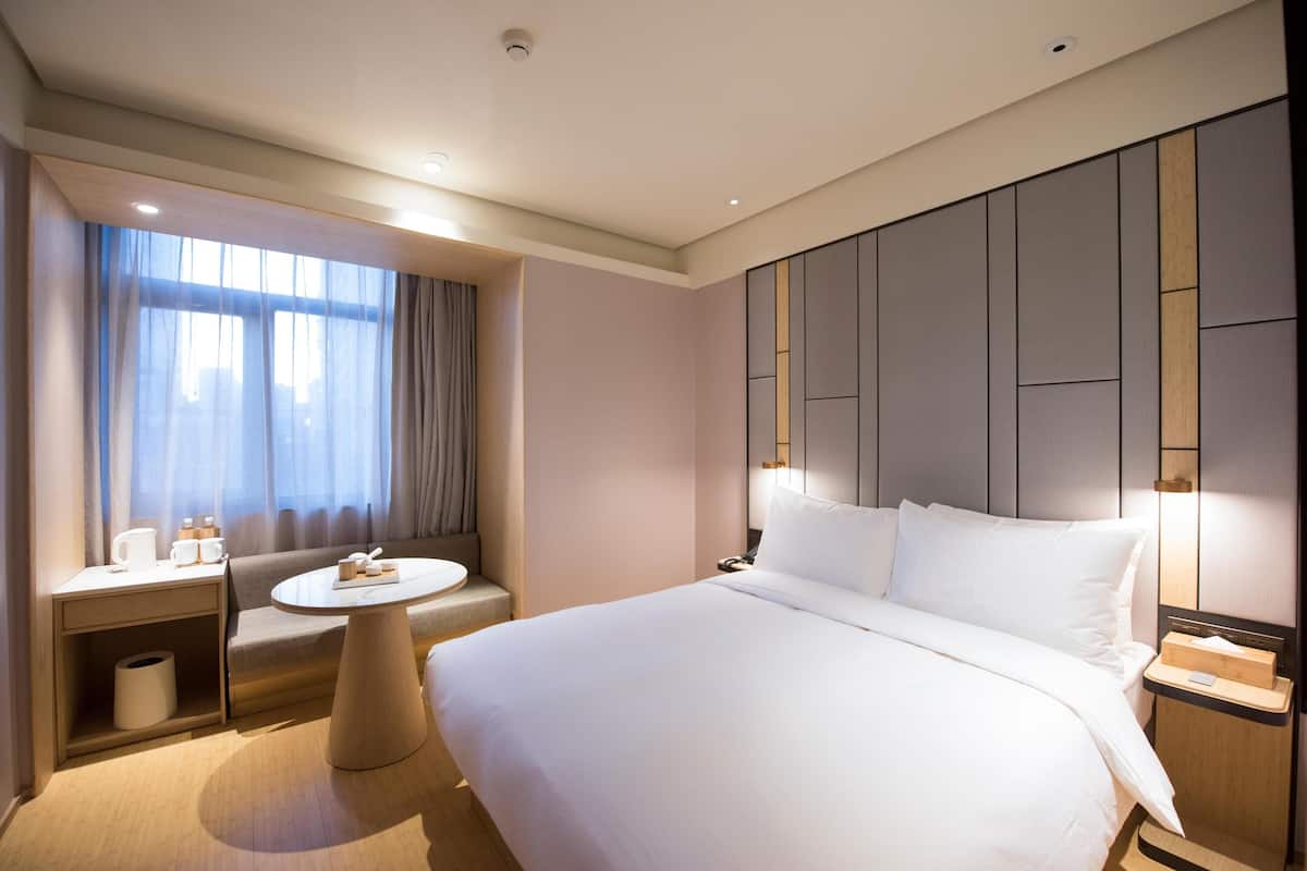 A hotel room with a large bed, a round table, a sofa, and a window with curtains.