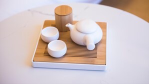 Una tetera blanca, dues tasses blanques i un recipient de fusta sobre un safata blanca.