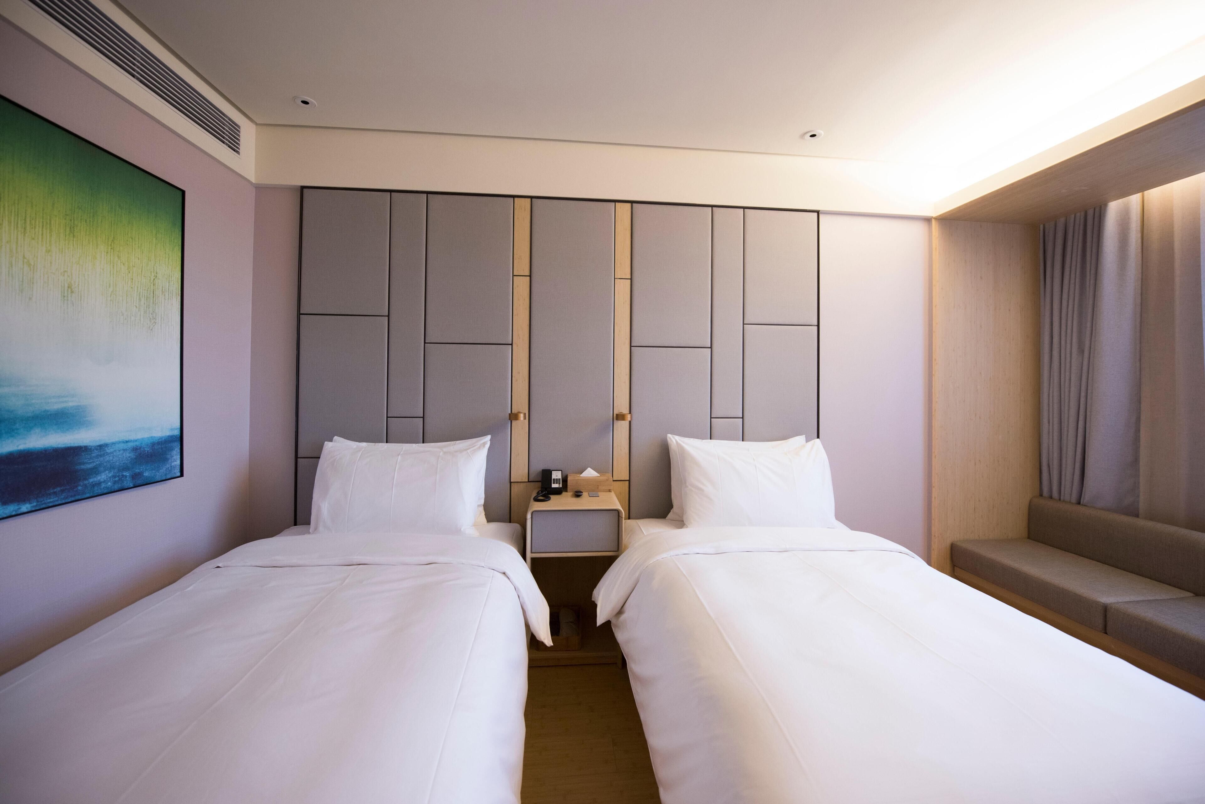 Habitación de hotel con dos camas, una mesita de noche, un cuadro y una zona de estar.