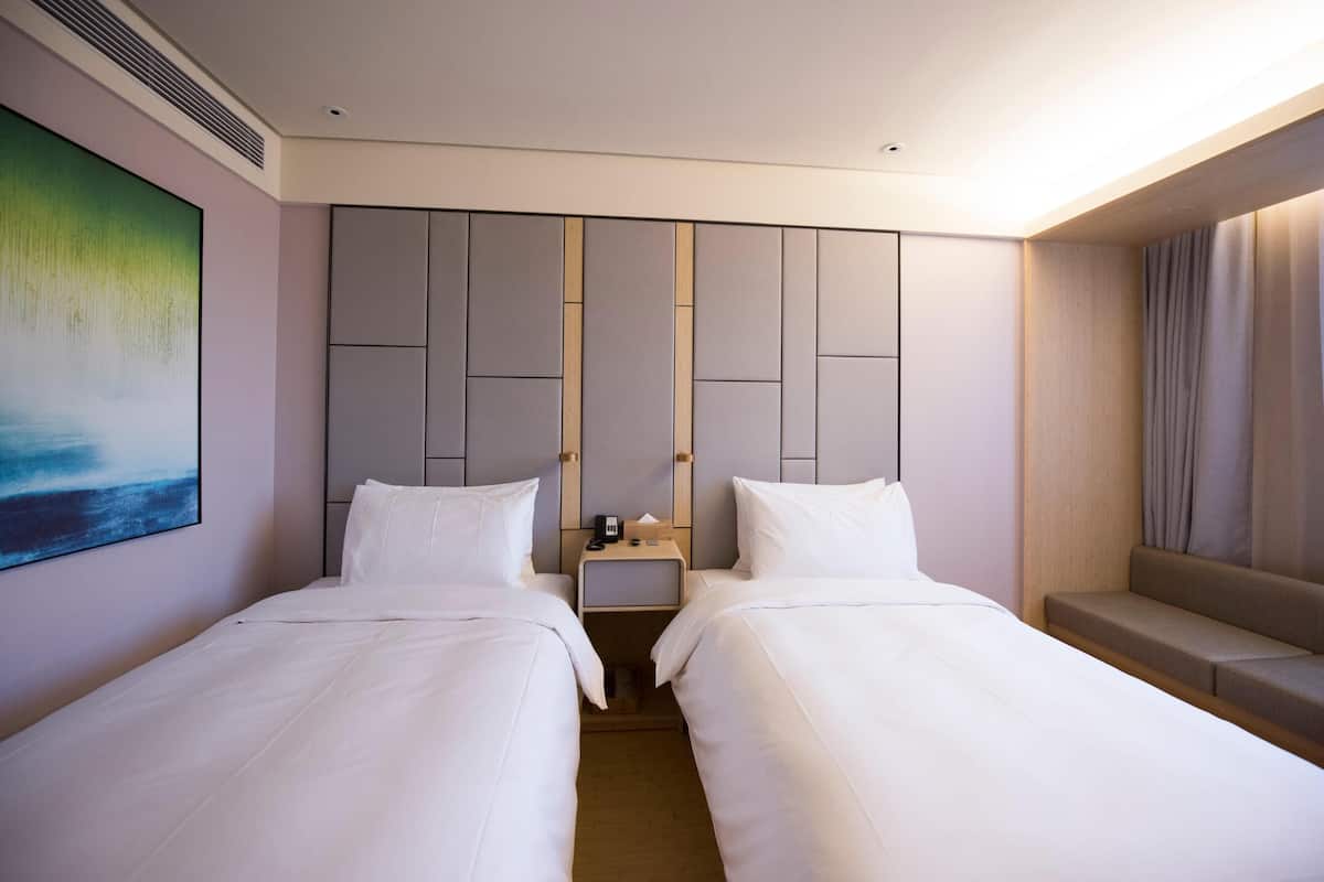 A hotel room with two beds, a nightstand, a painting, and a seating area.