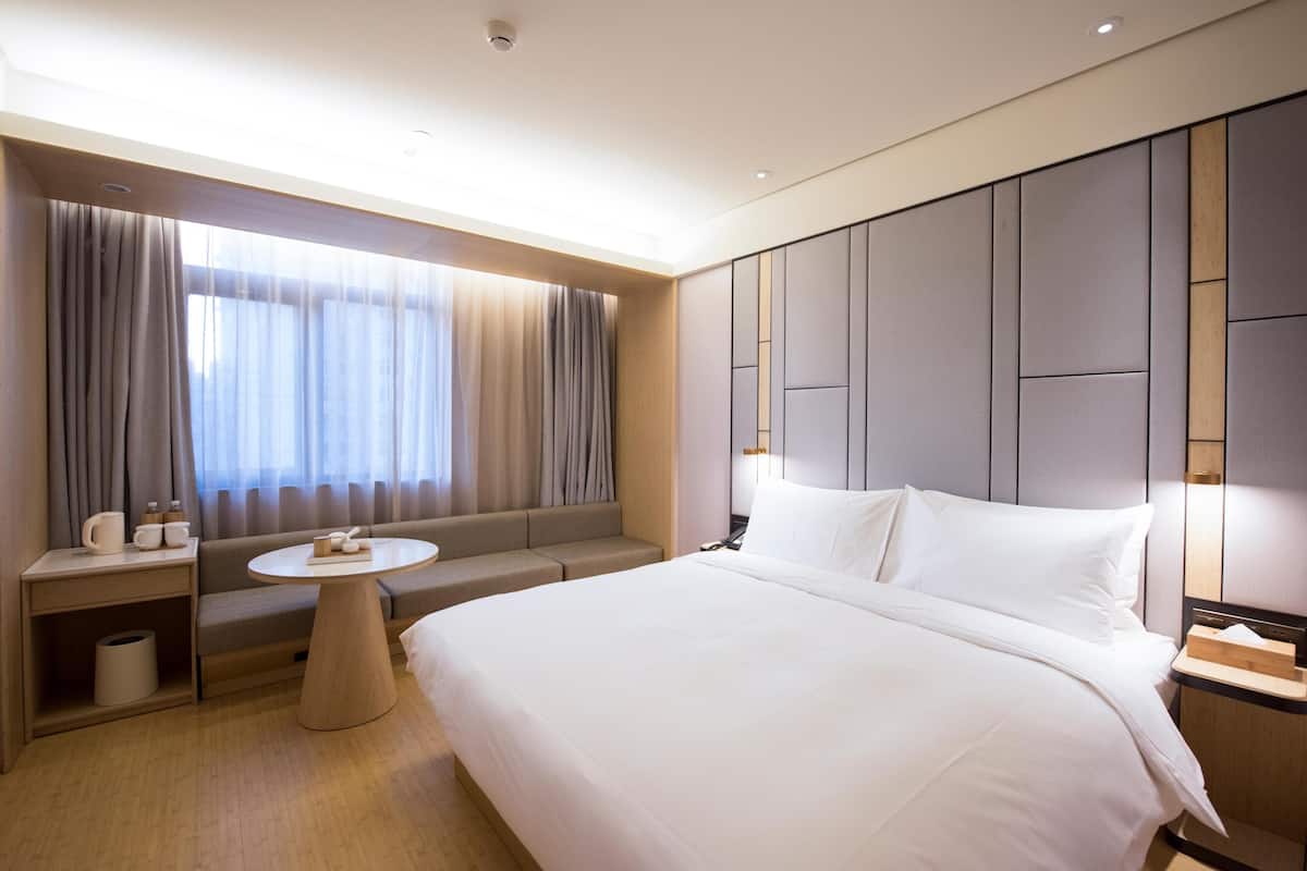 A hotel room with a large bed, a sofa, a small round table, and a window with curtains.
