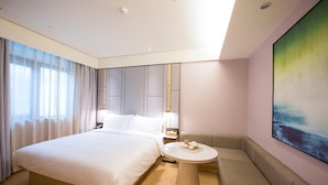 Habitació d'hotel moderna amb un llit gran, una taula rodona, un sofà i un quadre a la paret.