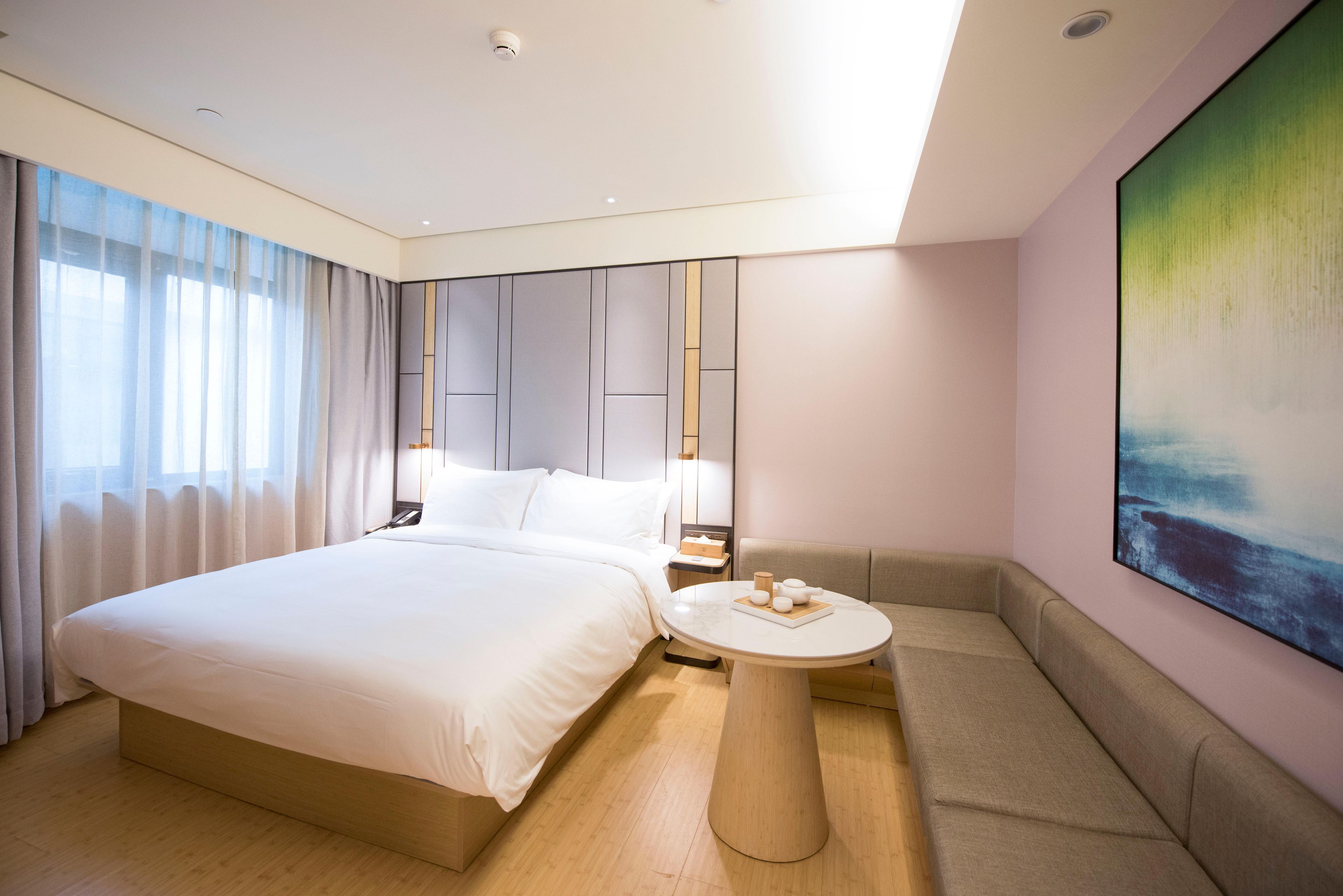 Habitación de hotel moderna con una cama grande, una mesa redonda, un sofá y un cuadro en la pared.