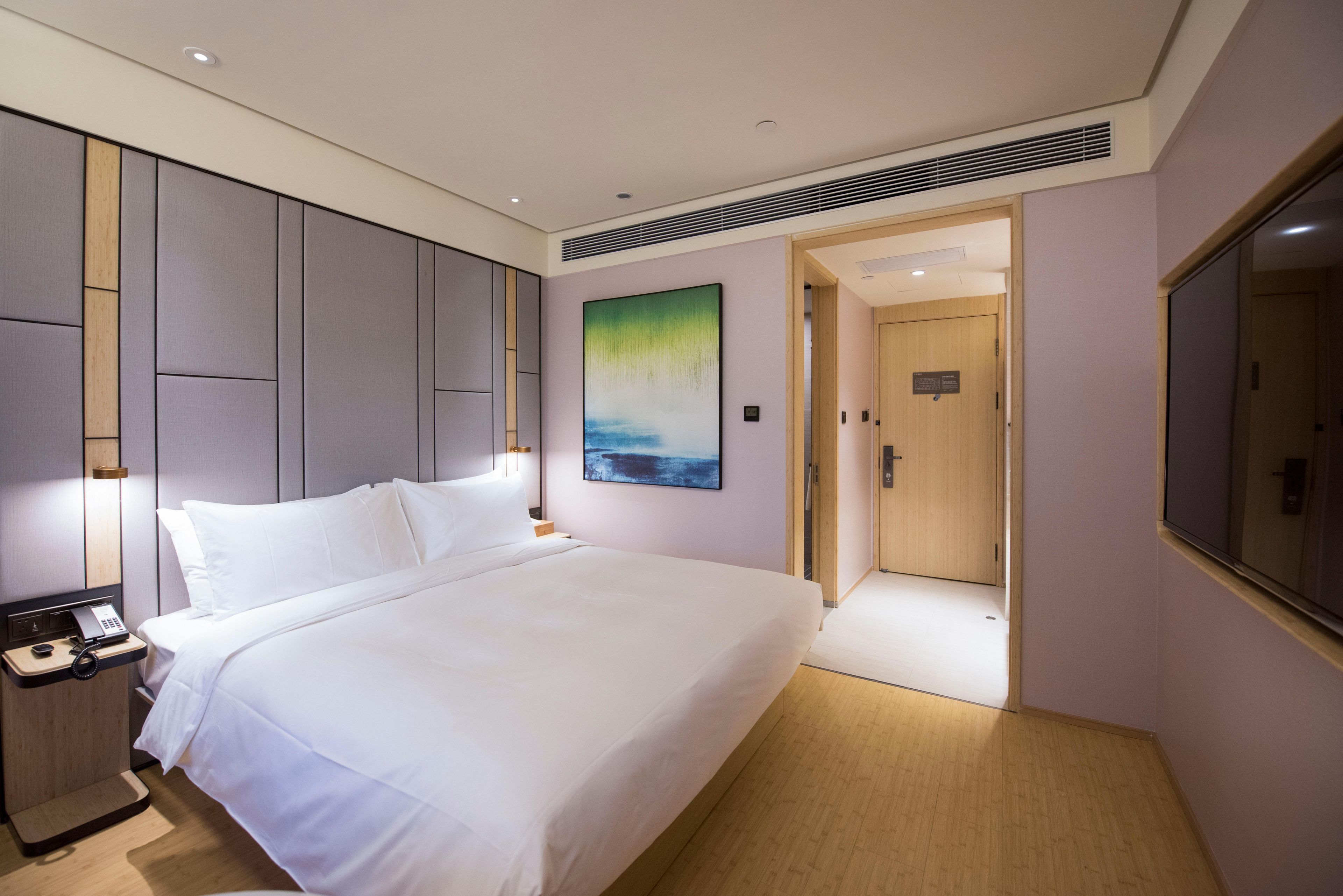 Habitación de hotel con una cama grande, mesita de noche con teléfono, un cuadro en la pared y una puerta que da a otra habitación.