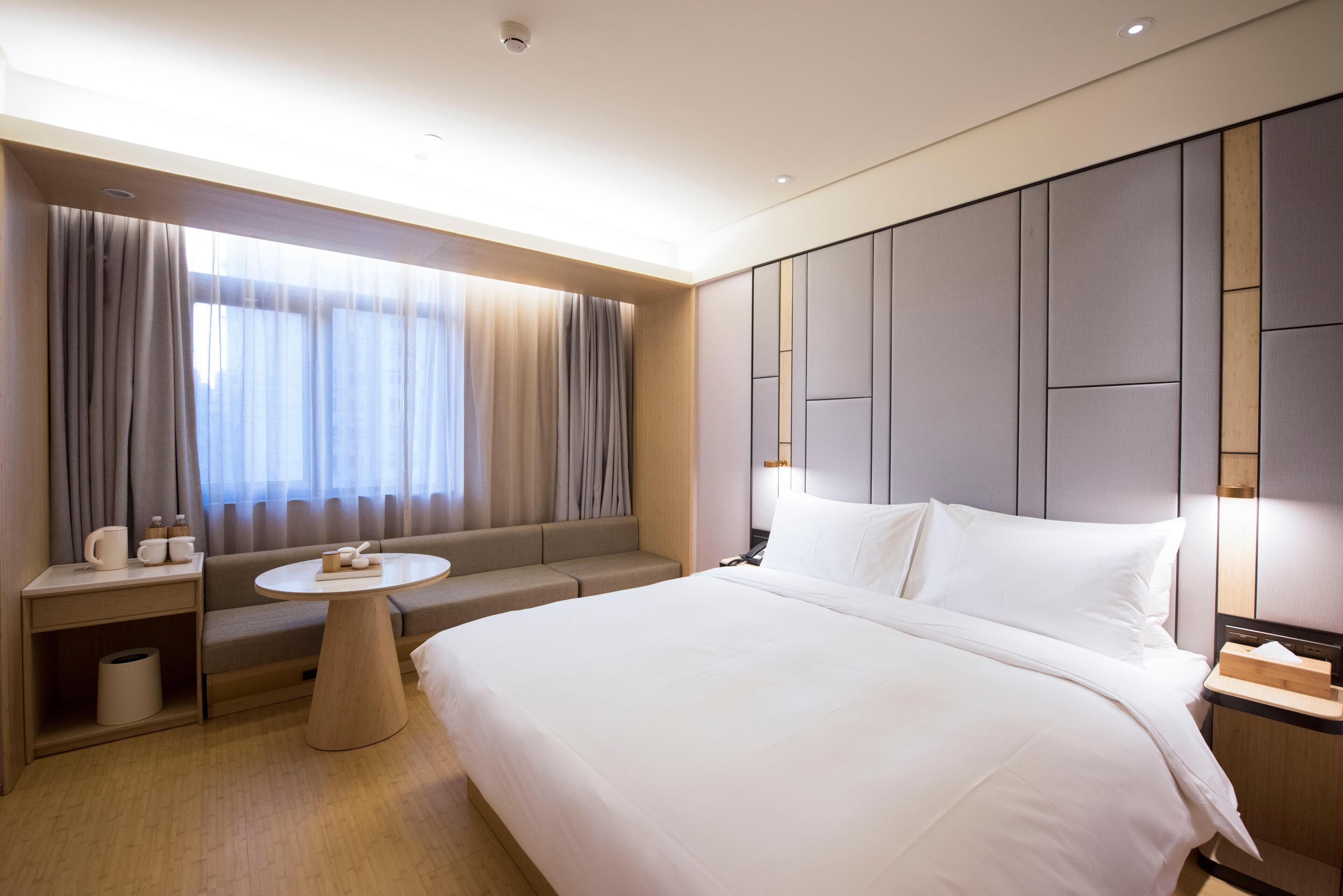 Una habitación de hotel con una cama grande, un sofá, una mesa redonda y una ventana con cortinas.