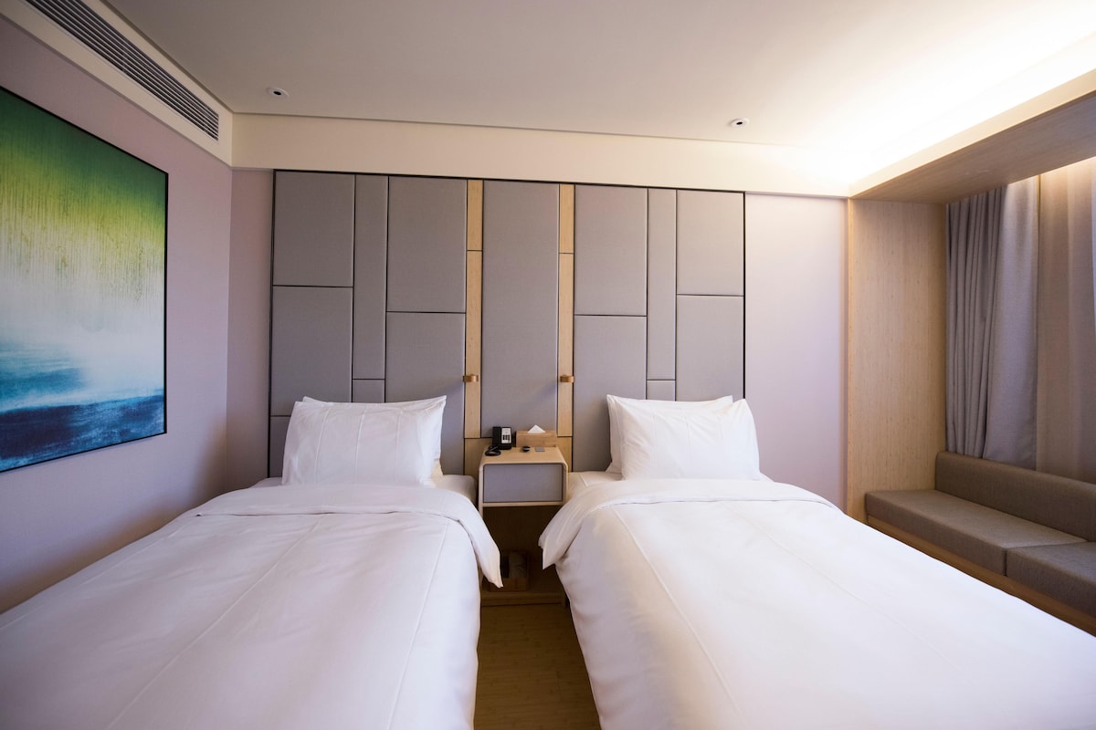 Habitación de hotel con dos camas, una mesita de noche, un cuadro y una zona de estar.