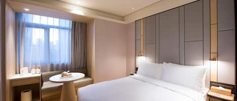 Quarto de hotel com uma cama grande, uma mesa redonda, um sofá e uma janela com cortinas.