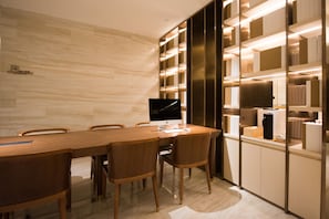 A modern dining area with a long wooden table, chairs, a flat-screen TV, and built-in shelving with books and decorative items.