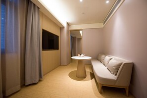 Una habitación de hotel moderna con suelo de madera, una mesa redonda con juego de té, un sofá y un ventanal con cortinas.
