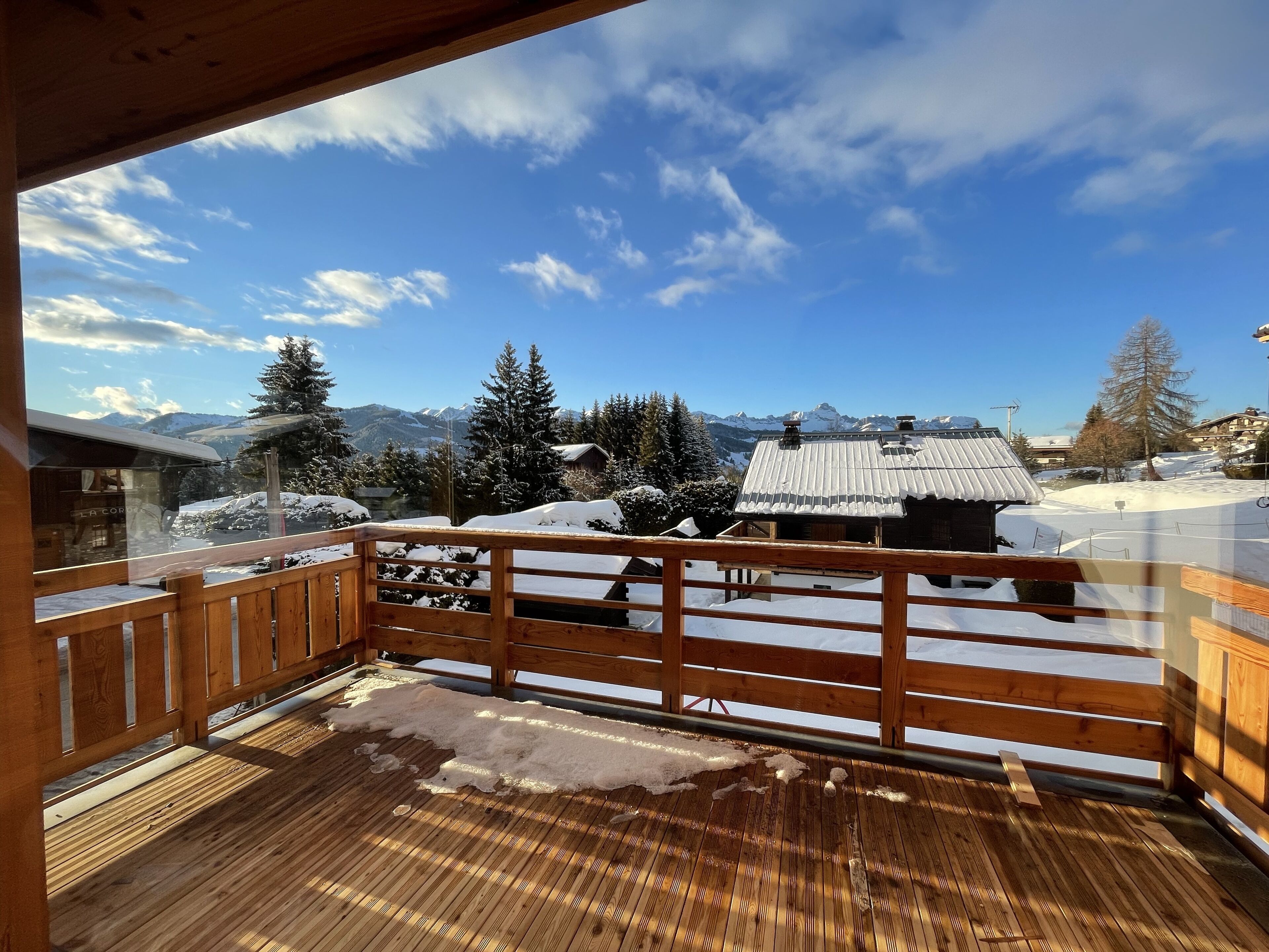 Une terrasse en bois offrant une vue sur des montagnes enneigées et un chalet.