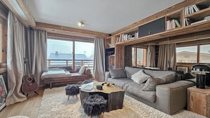 A cozy living room with a large window, a sofa, a coffee table, and a bookshelf. - Standing megeve - 2 to 8 people - Mont Arbois - ⛷️ and 🏌️‍♀️ (Megeve)