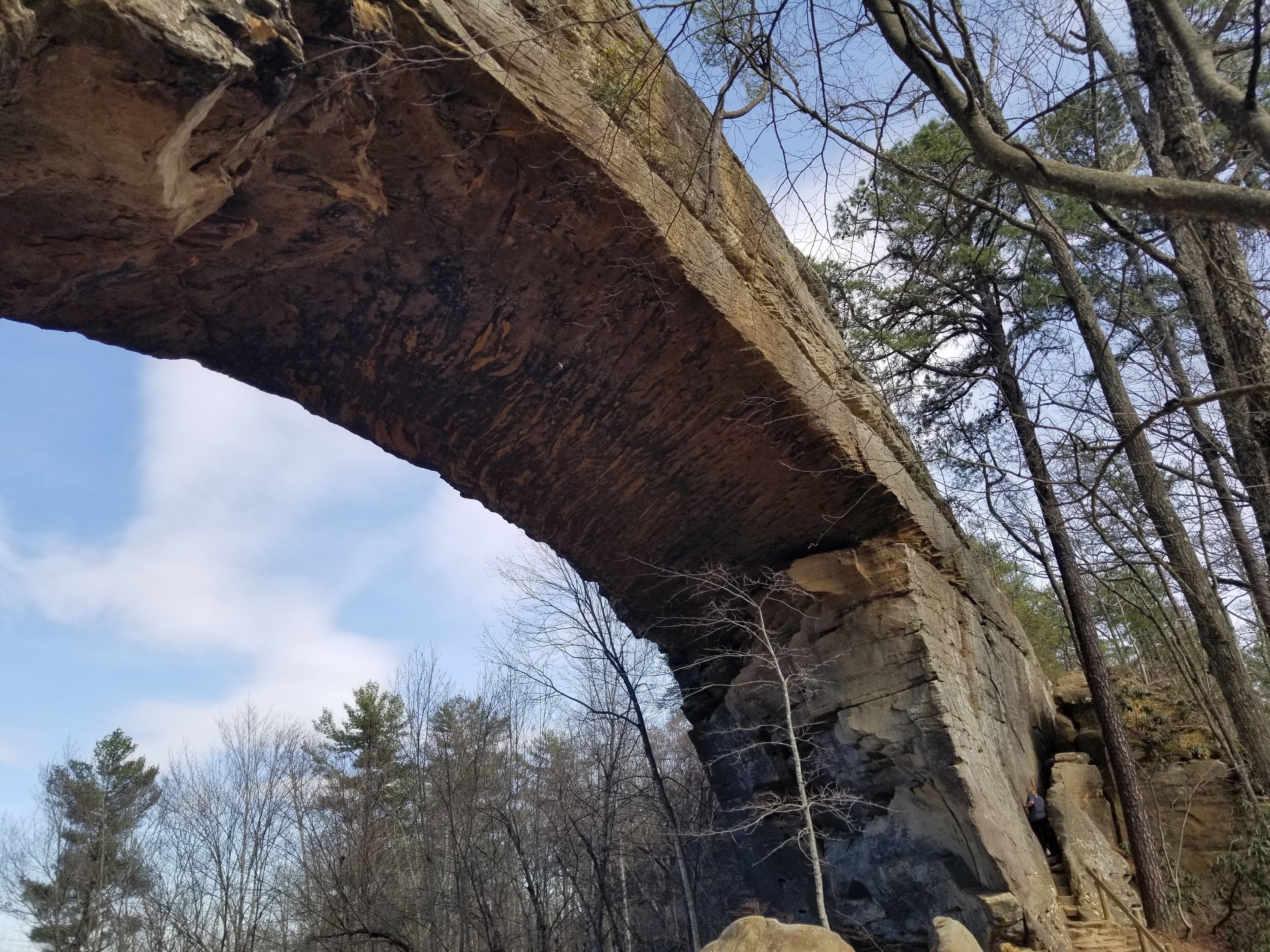 Un'imponente formazione rocciosa ad arco con una persona che scala una parete rocciosa nelle vicinanze.