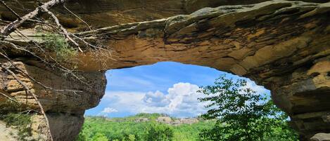 A natural rock arch formation with a view of a forested valley below.