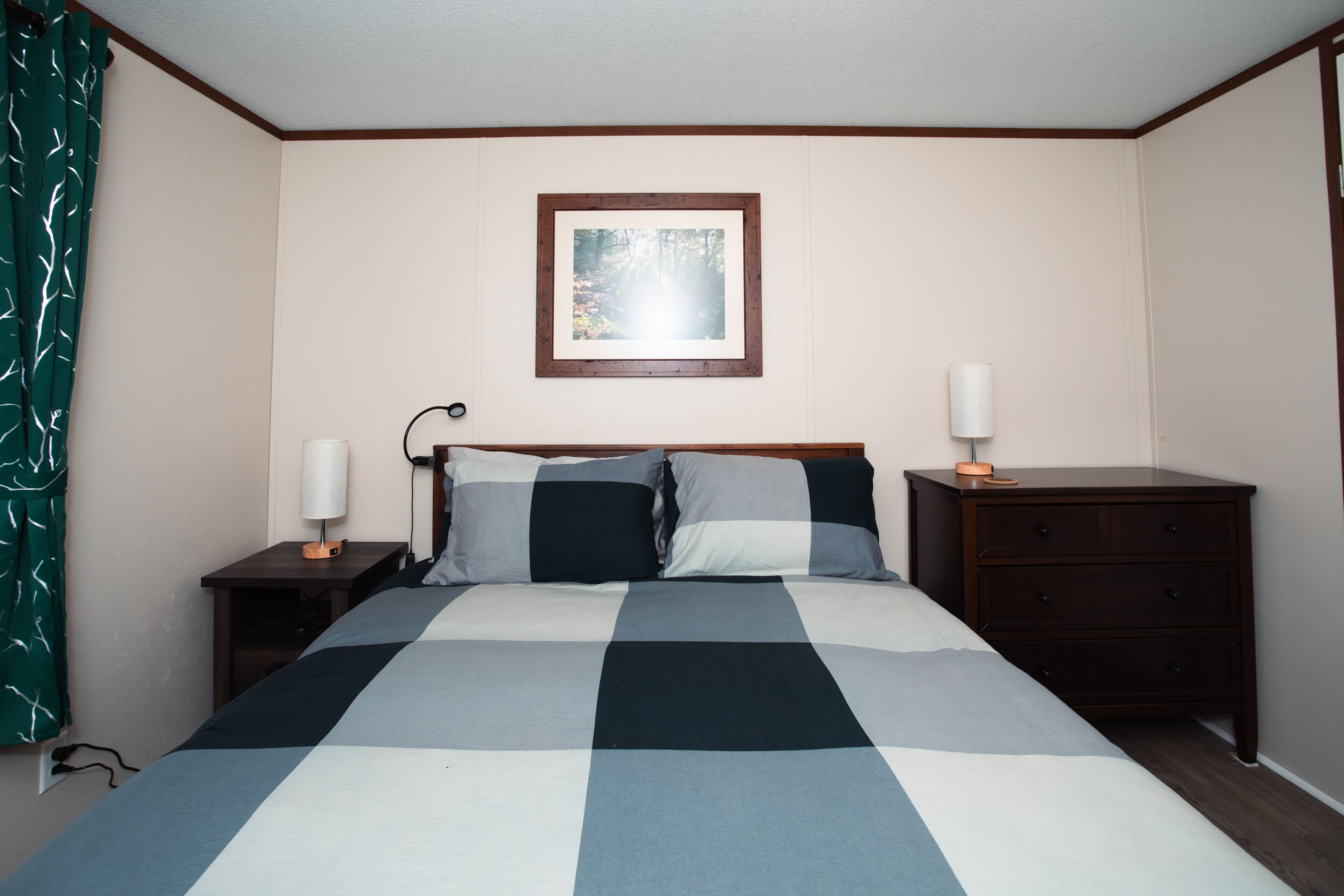 A bedroom with a bed, two bedside tables, a nightstand, a dresser, a framed picture on the wall, and a curtain.