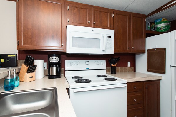 A kitchen with wooden cabinets, a white stove, a microwave, and a refrigerator.
